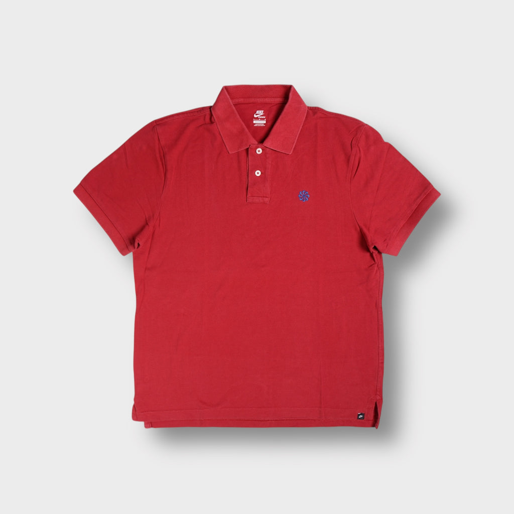 Nike polo shirt in red featuring a blue embroidered sunburst logo on the chest