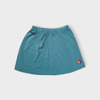 Blue Nike tennis skirt featuring a colourful Nike Court logo patch near the hem.