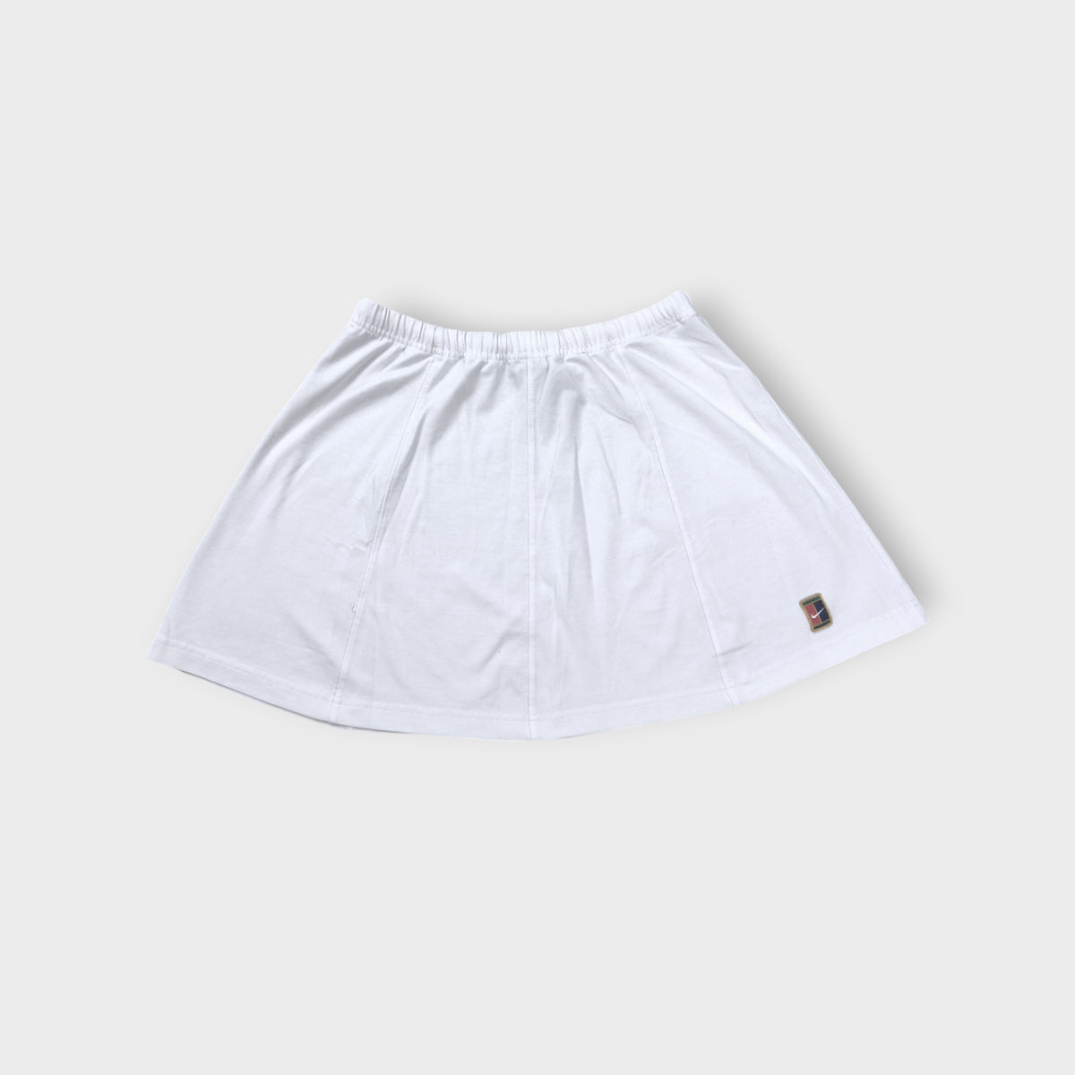 Nike mini tennis skirt in white with a colorful embroidered court logo patch near hem