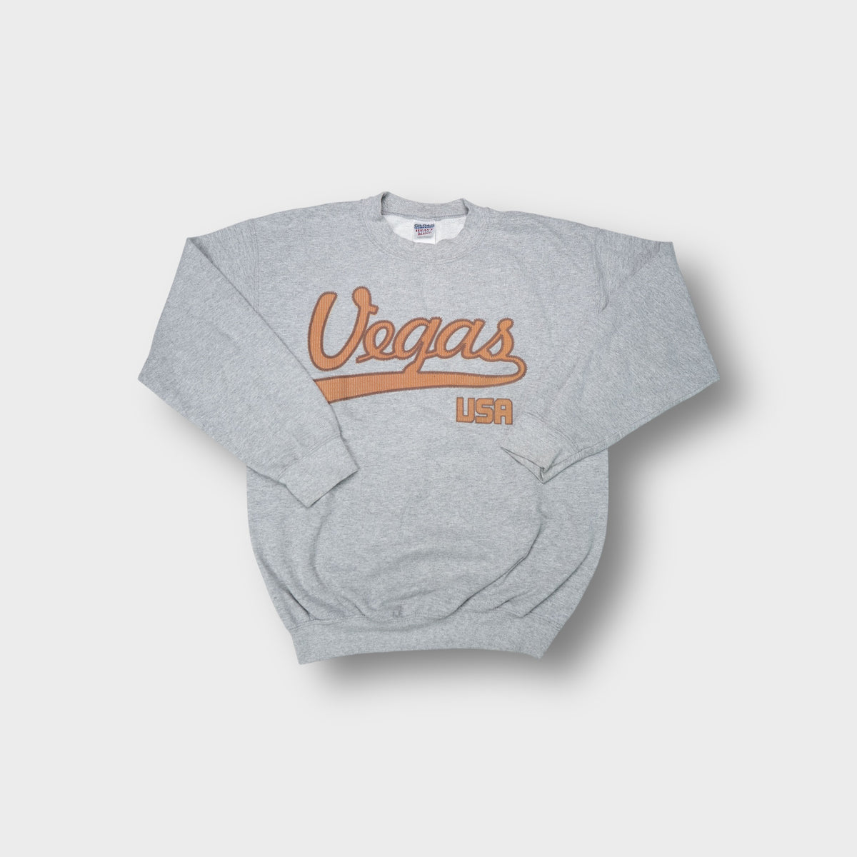 Gildan crew-neck sweater in grey featuring brown script Vegas USA lettering across the chest