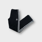 Black Adidas trackpants with white three stripes down the legs and trefoil logo embroidery