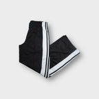 Adidas black trackpants with white side stripe panels and woven logo patches on the leg.