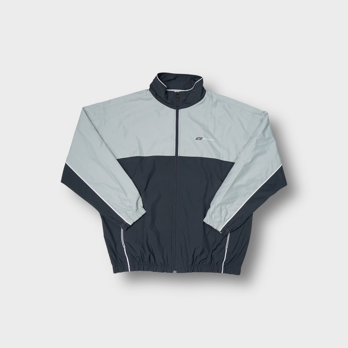 Reebok track jacket in grey and dark navy featuring a small chest logo.
