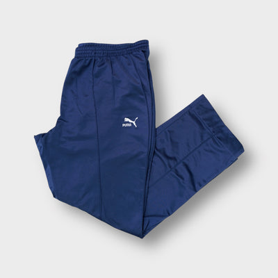 Puma blue trackpants featuring an embroidered white cat logo and stitched pleats.