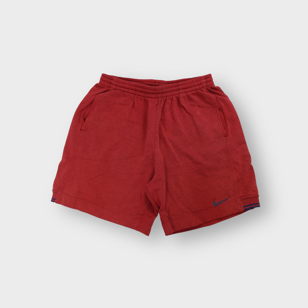 Red Nike fleece shorts featuring a small blue embroidered swoosh on the leg