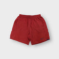 Red Nike fleece shorts featuring a small blue embroidered swoosh on the leg
