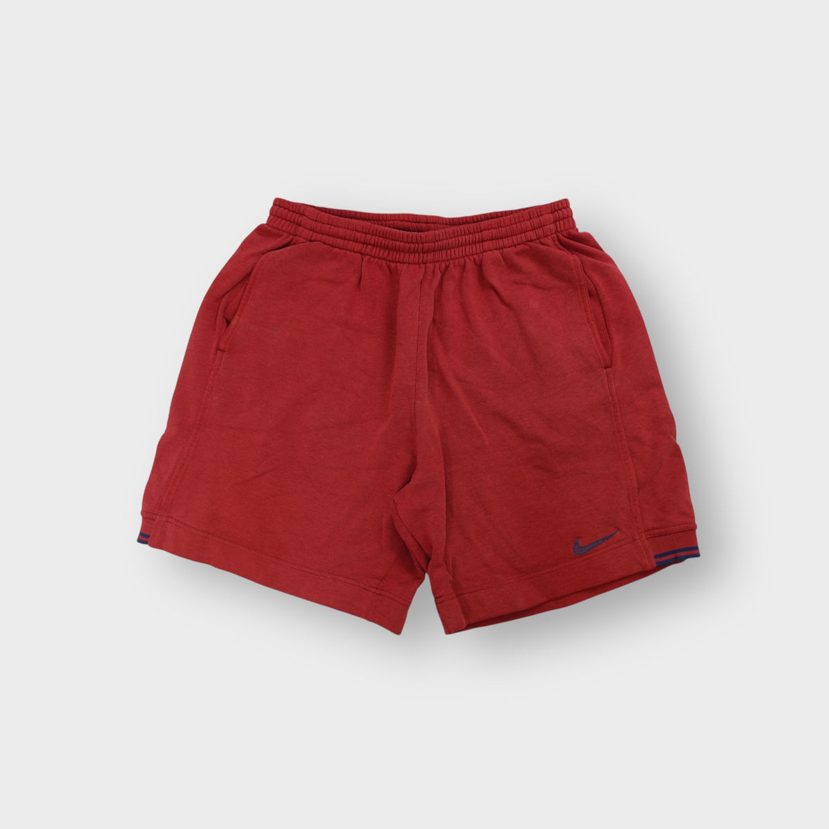 Red Nike fleece shorts featuring a small blue embroidered swoosh on the leg