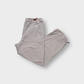Nike trackpants in beige featuring red drawstring waist toggles and an orange swoosh logo.