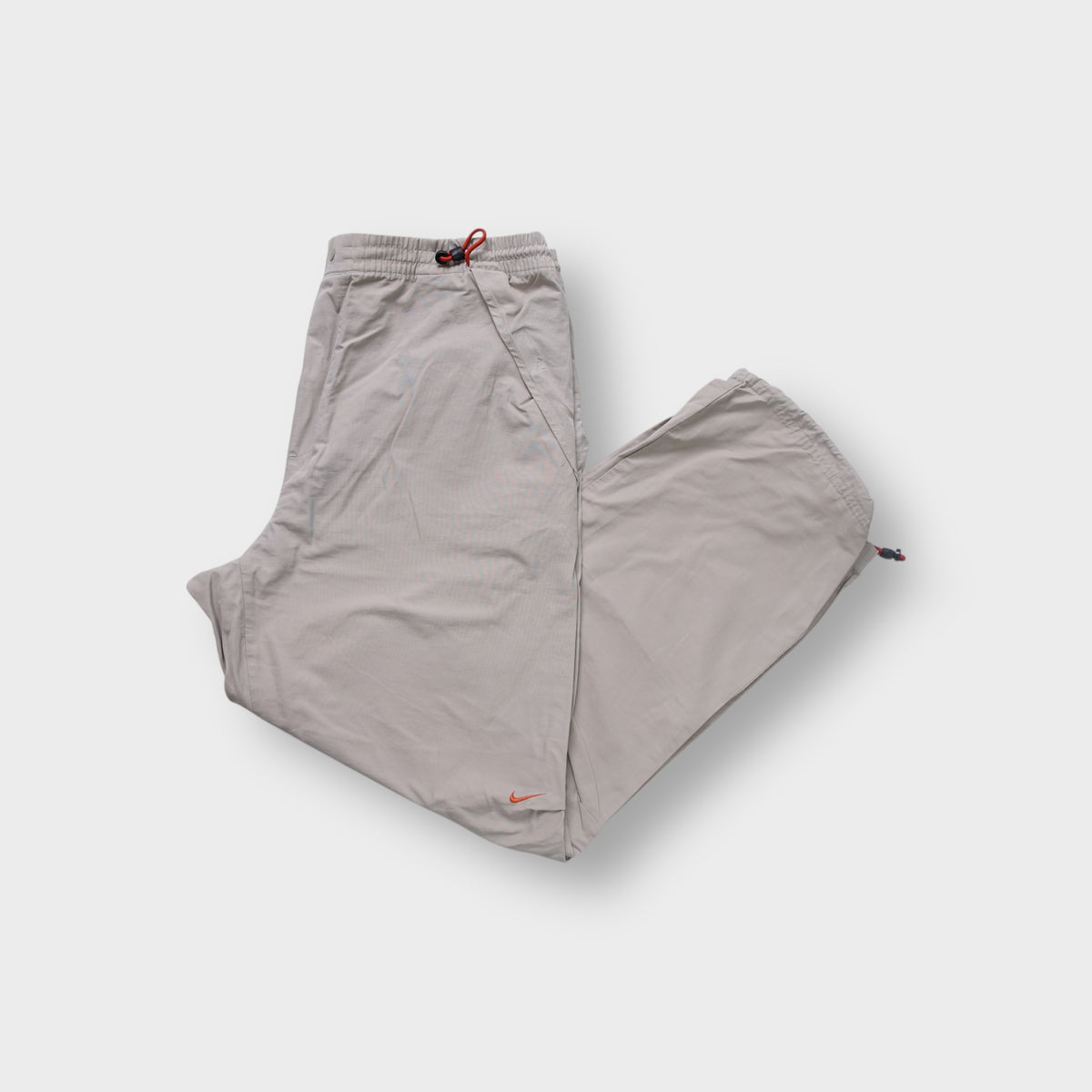 Nike trackpants in beige featuring red drawstring waist toggles and an orange swoosh logo.
