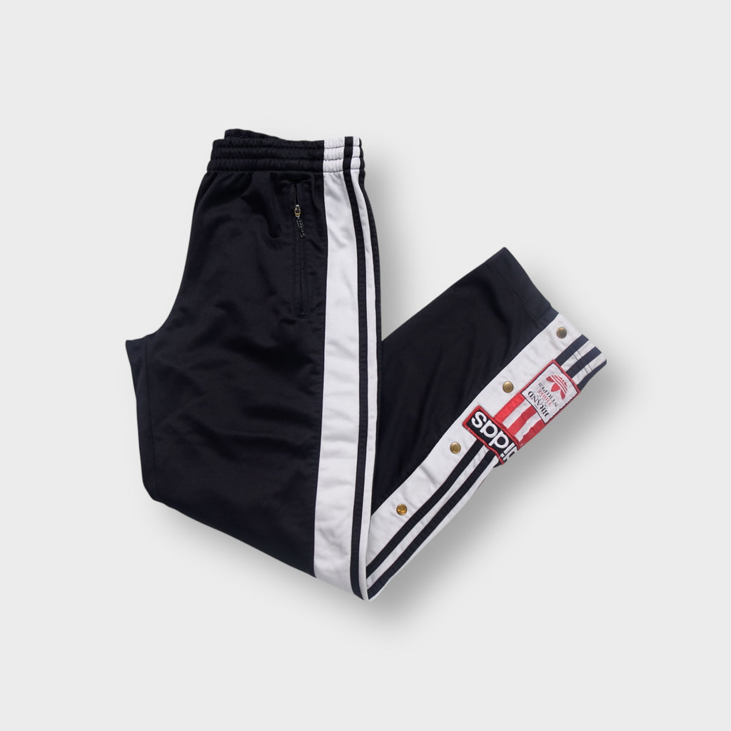 Black Adidas trackpants with white stripe panels, snap buttons, and an embroidered patch.