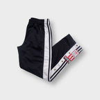 Black Adidas trackpants with white stripe panels, snap buttons, and an embroidered patch.
