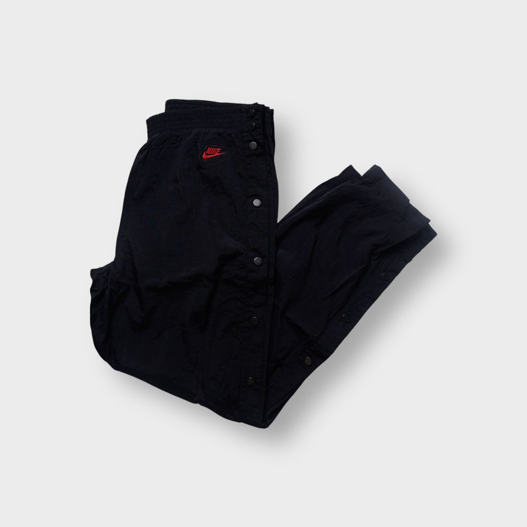 Black Nike trackpants featuring side snap buttons and a red embroidered logo
