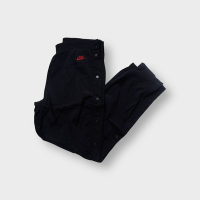 Black Nike trackpants featuring side snap buttons and a red embroidered logo