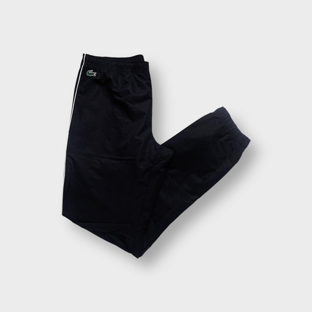 Lacoste black trackpants featuring white side piping and a green crocodile patch near the waist