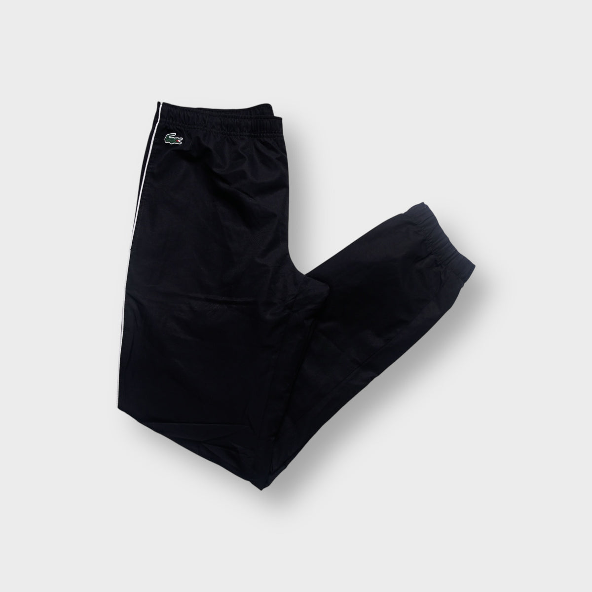Lacoste black trackpants featuring white side piping and a green crocodile patch near the waist