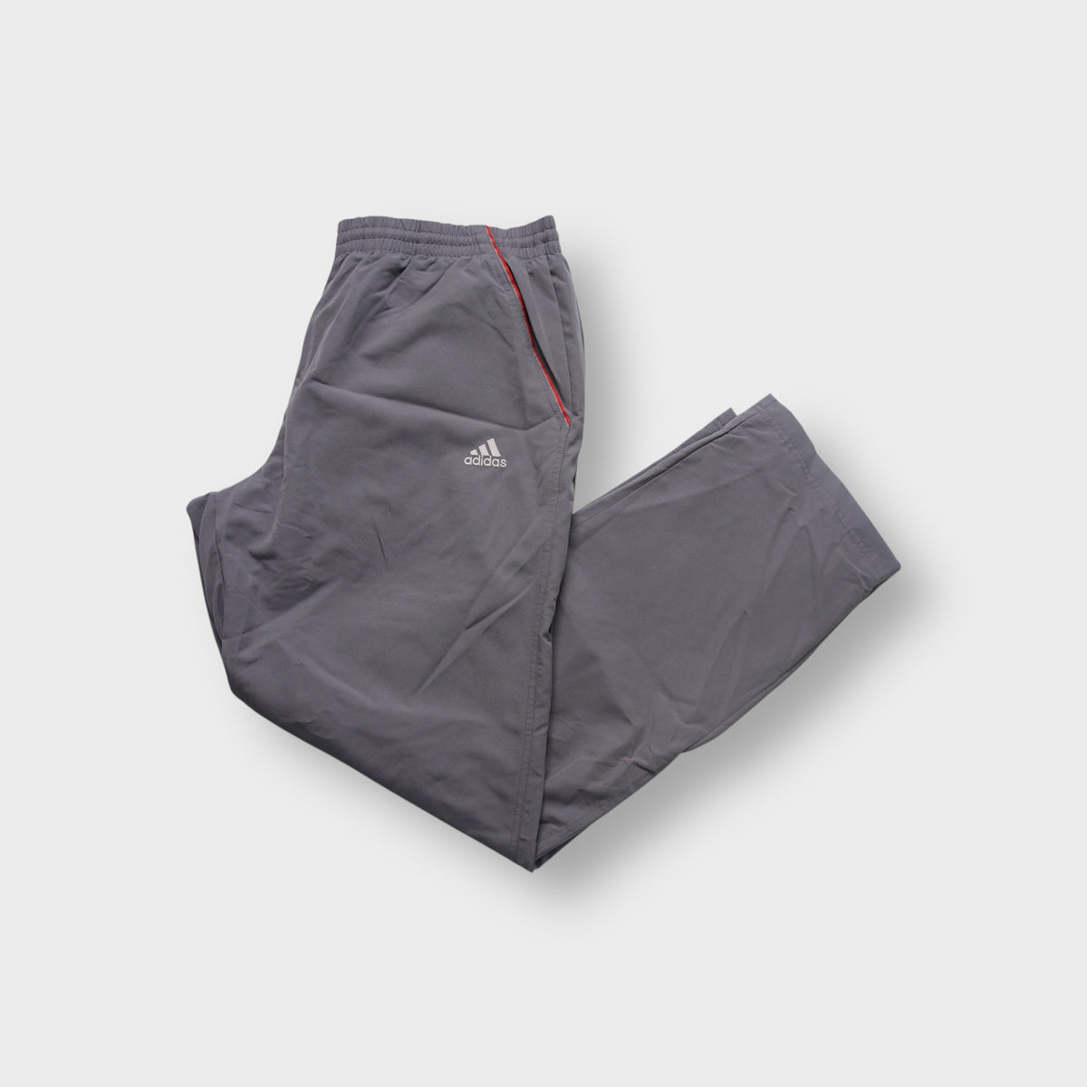 Grey Adidas trackpants showing red side piping and embroidered logo