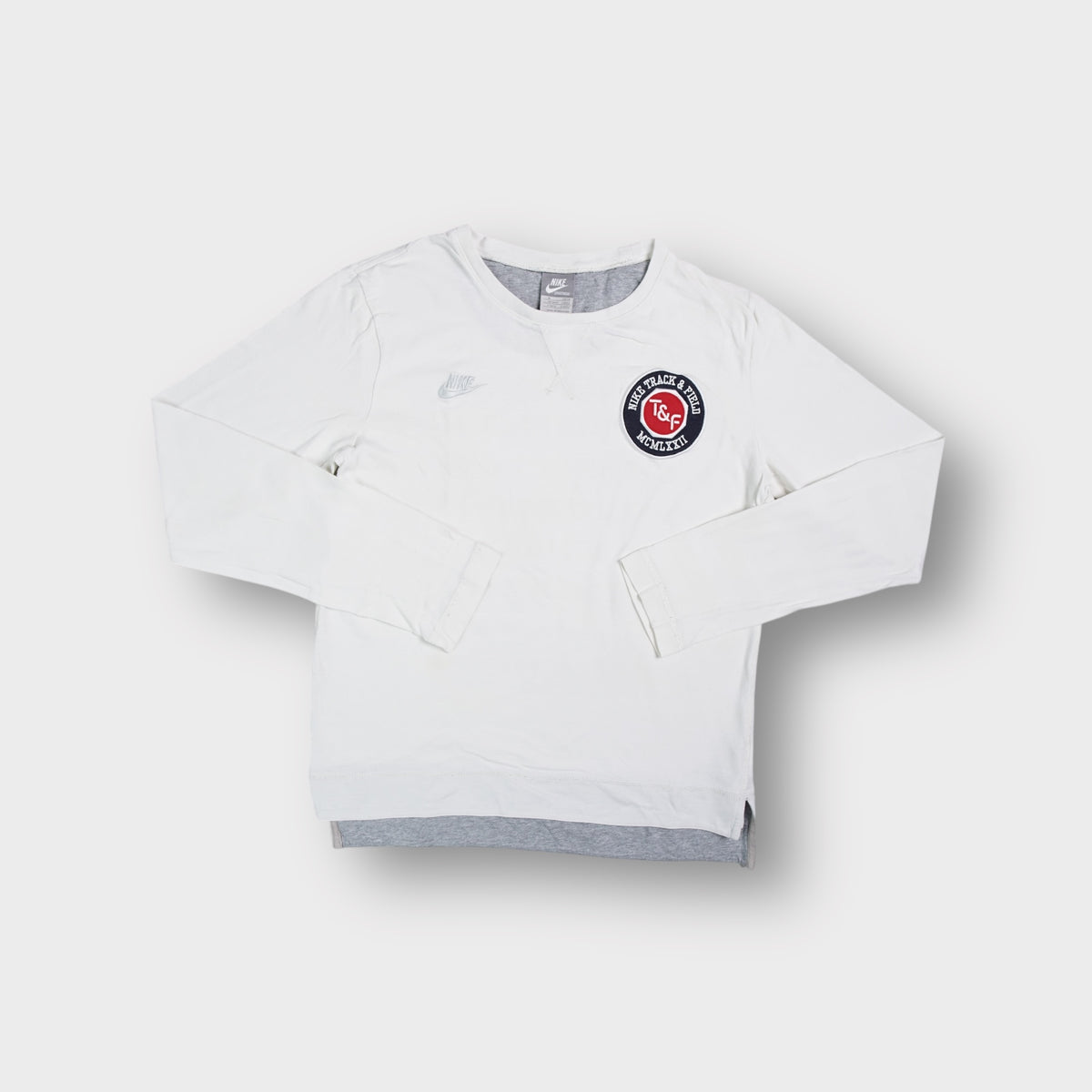 White Nike long-sleeve sweater featuring a round Track and Field logo patch
