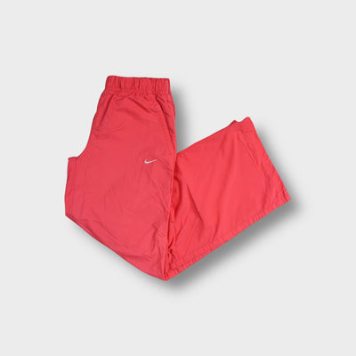 Pink Nike trackpants featuring a small white embroidered Swoosh logo on the upper left hip