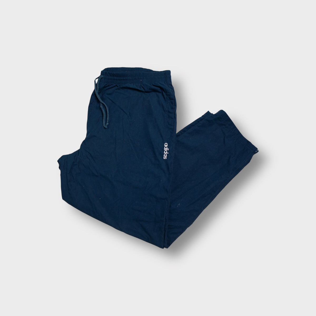 Navy blue Adidas trackpants featuring a small white embroidered logo on the upper leg