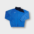 Nike blue track jacket with embroidered white Swoosh logo and dark blue shoulder patch.