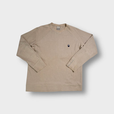 Beige Nike ribbed knit sweater featuring a small oval swoosh patch on the chest