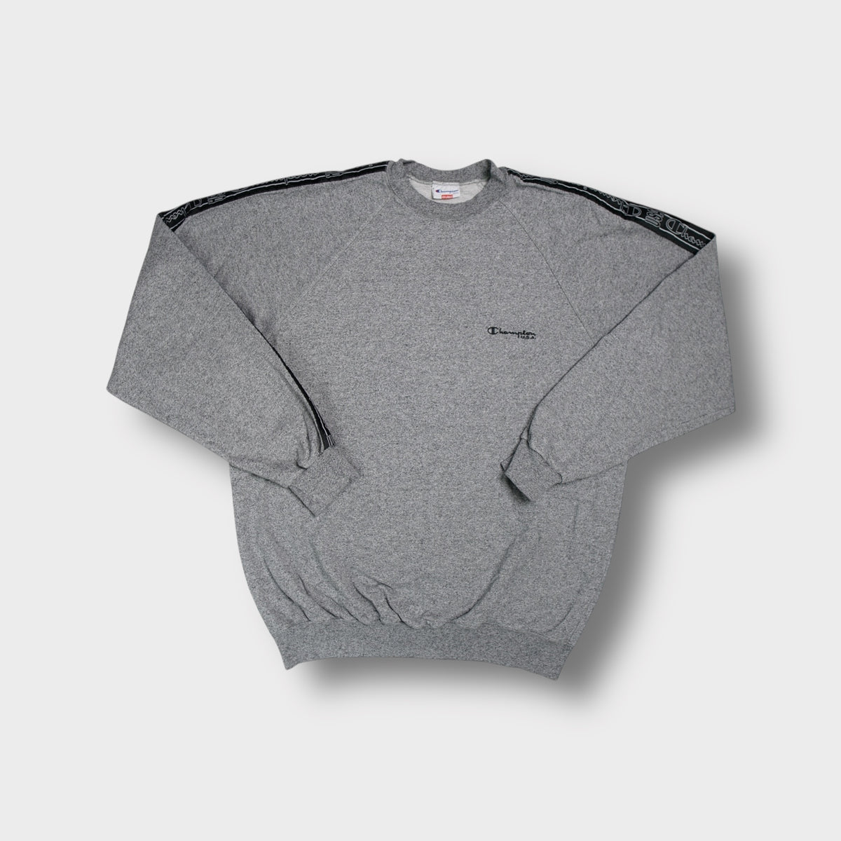 Champion grey crew-neck sweater featuring black logo tape trim along the sleeves.