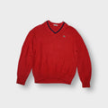 Red Lacoste V-neck knit sweater featuring navy blue trim and an embroidered crocodile logo on the chest.