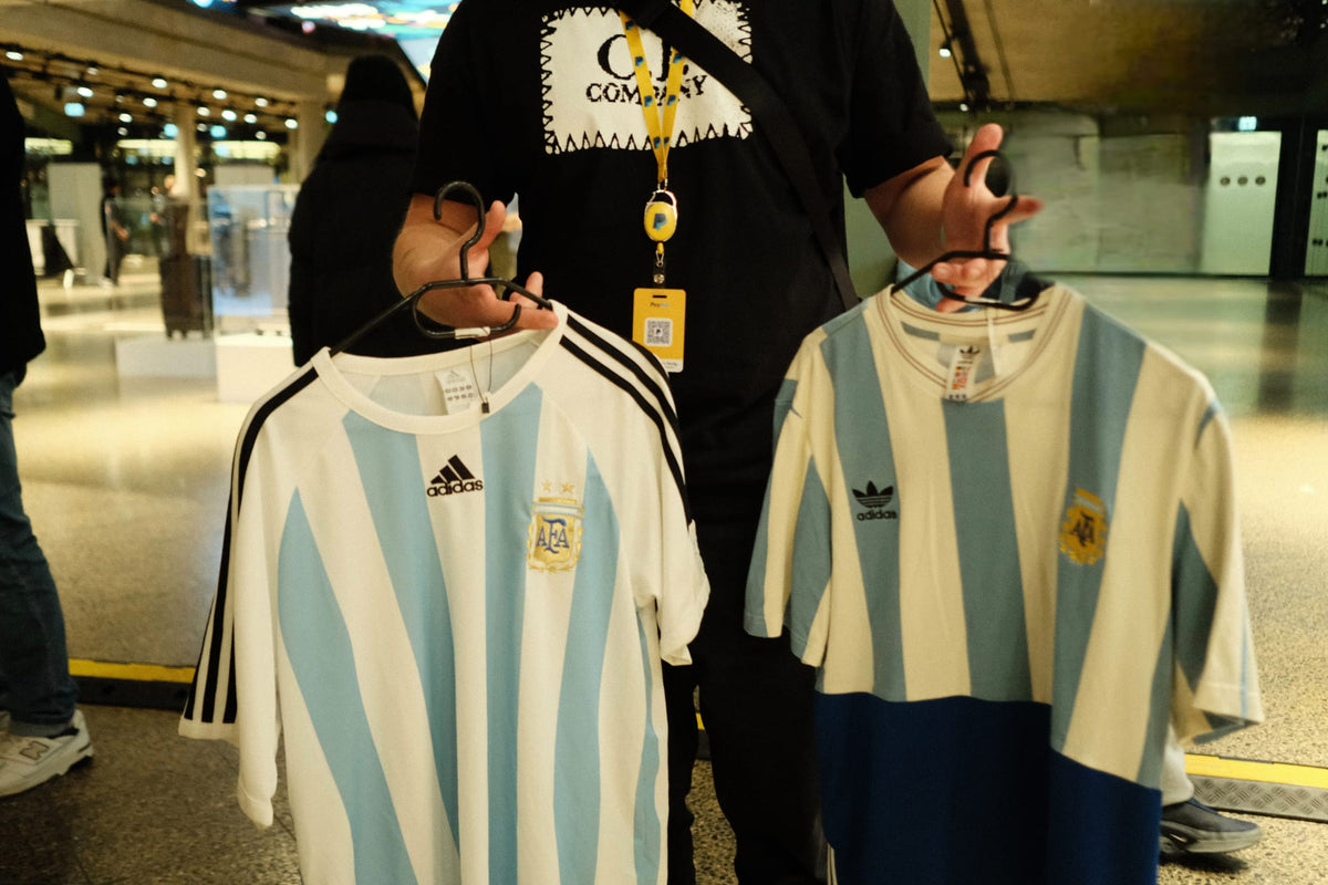 Two vintage Argentina football shirts held up on hangers at a vintage fair.