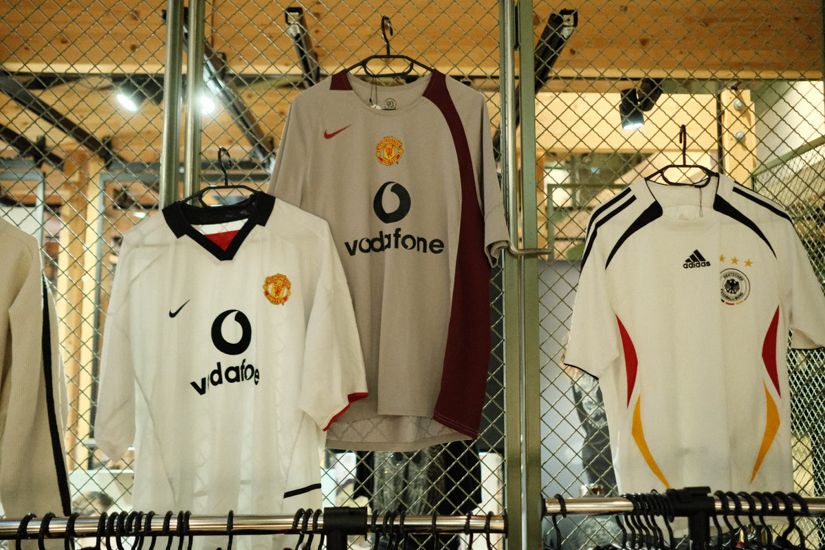 Three 90s and 2000s football shirts on a rail: two white Manchester United jerseys and a white Germany shirt.