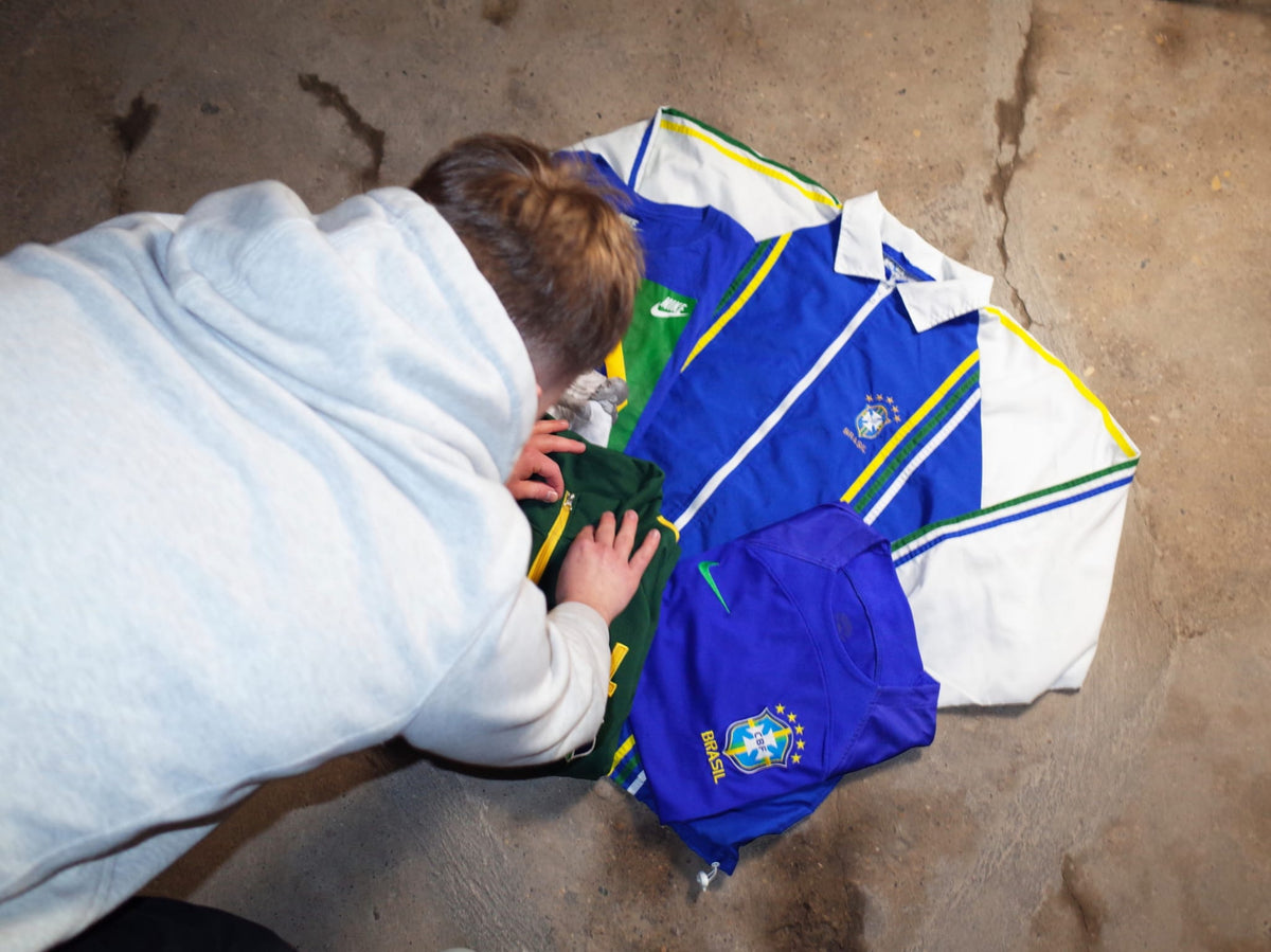 Seen from above: vintage Brazil football shirts being sorted on a concrete floor.