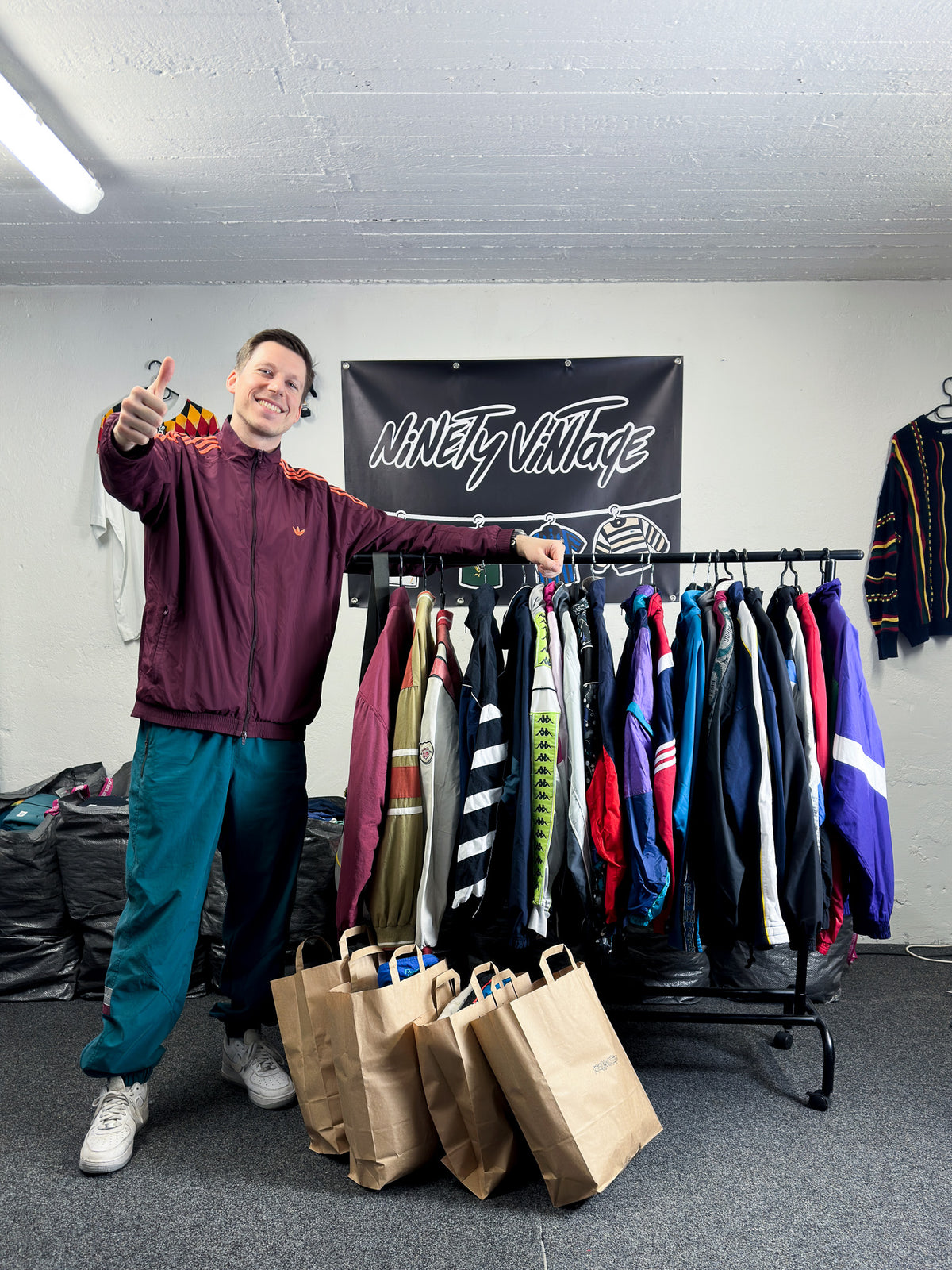 Björn von Morgenstern in a burgundy Adidas track jacket and teal track pants, next to a rail of vintage track jackets and ninetyvintage bags.