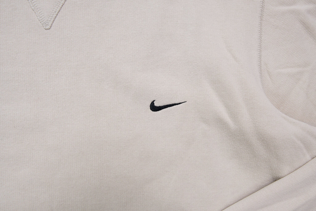 Nike crewneck sweater in beige featuring a small black embroidered Swoosh logo on the chest, detail