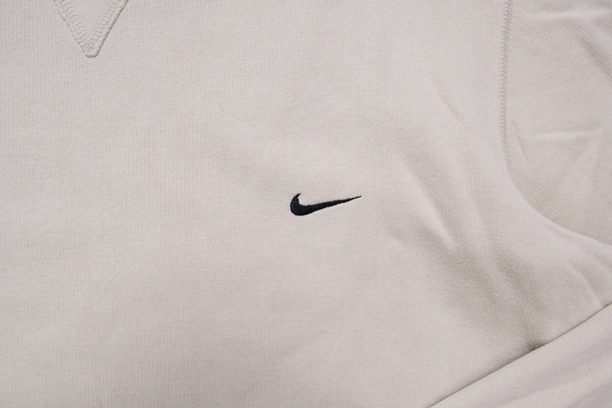 Nike crewneck sweater in beige featuring a small black embroidered Swoosh logo on the chest, detail