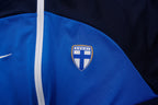 Nike track jacket in blue and navy featuring the Suomi crest on the chest, detail