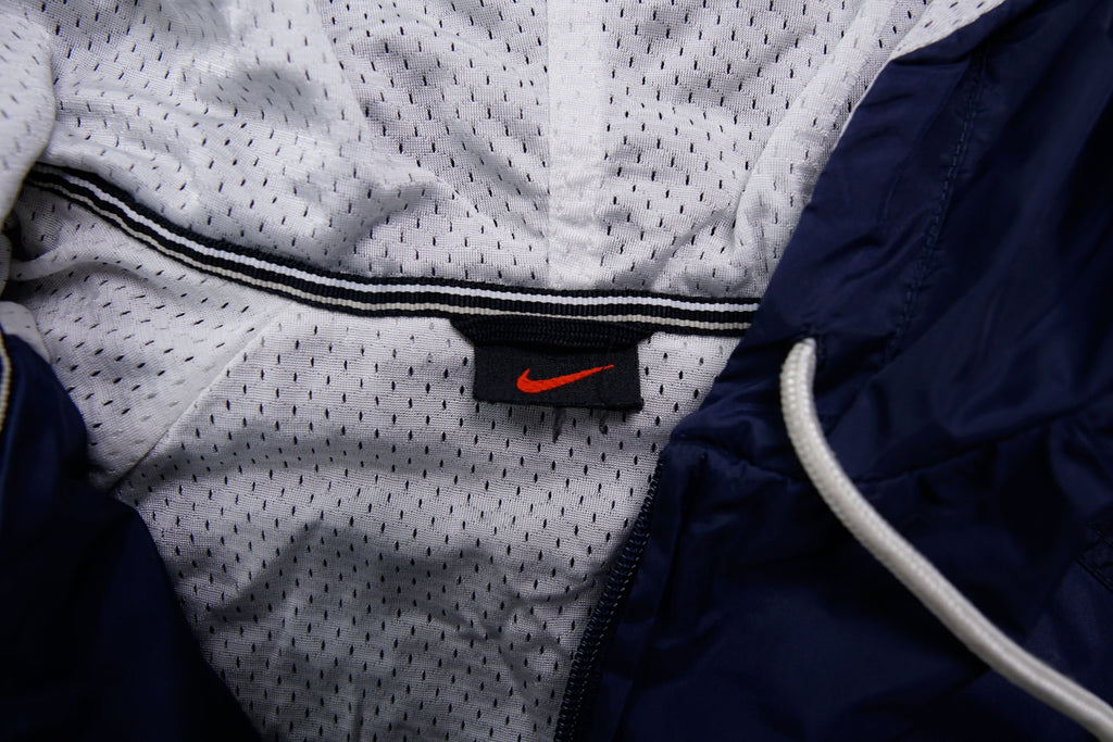 Nike navy jacket featuring a white chest stripe, hooded half-zip, and small embroidered swoosh, size label