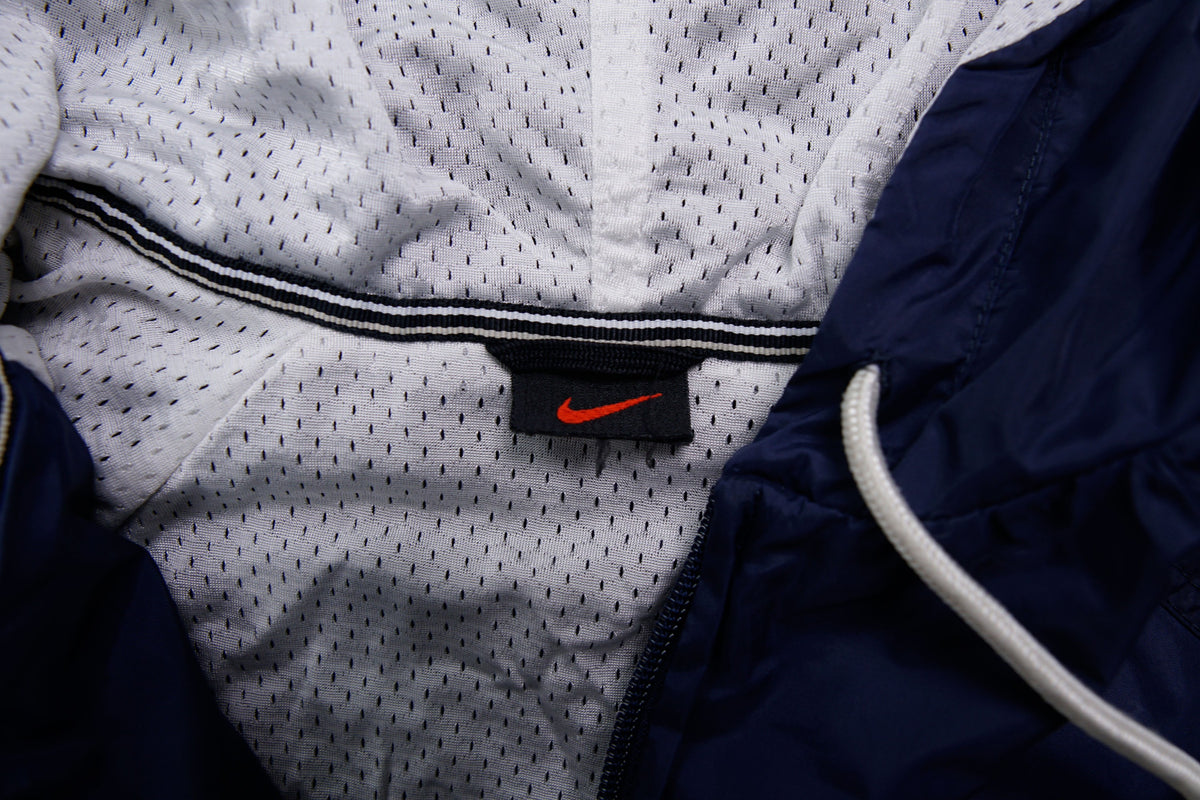 Nike navy jacket featuring a white chest stripe, hooded half-zip, and small embroidered swoosh, size label