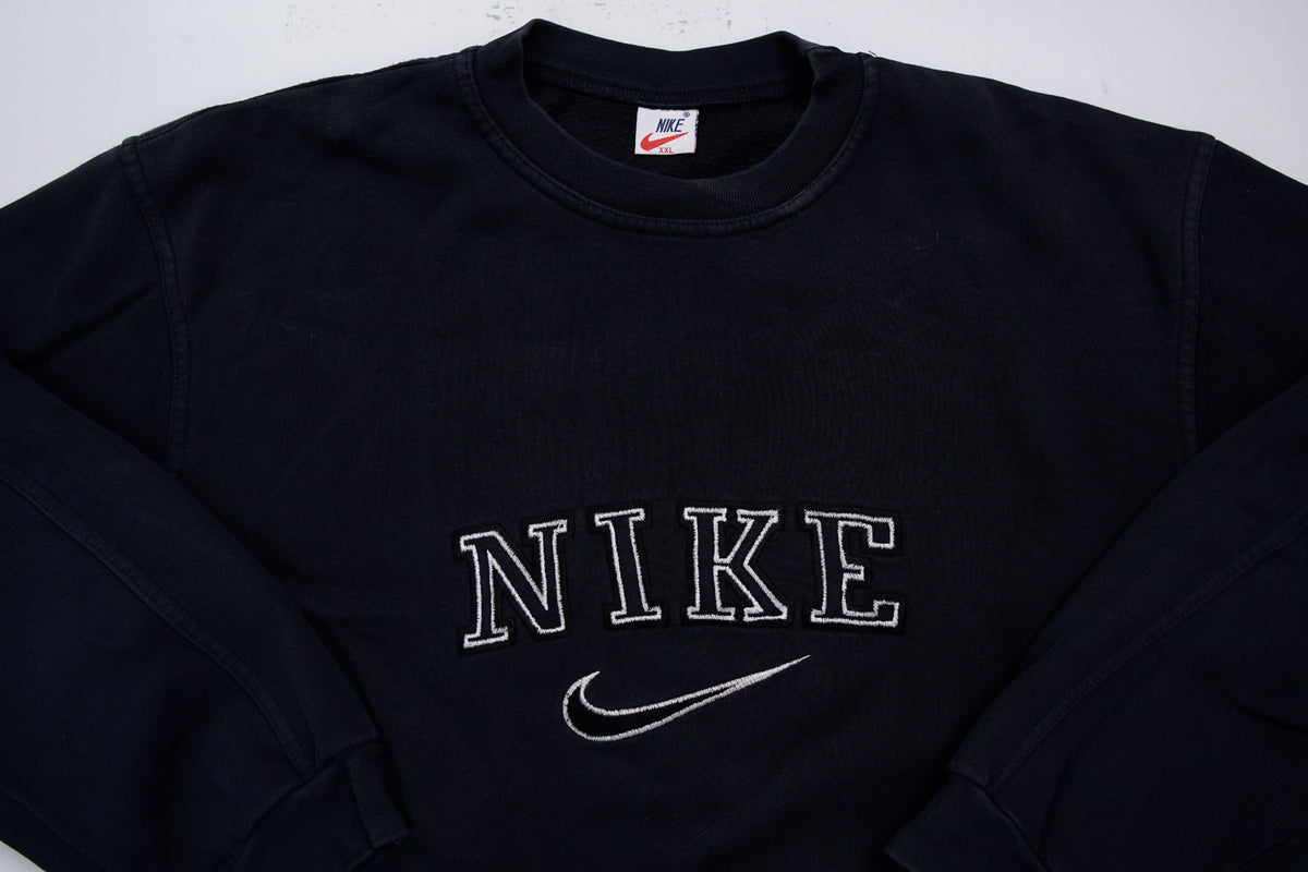 Black Nike sweater with embroidered white spellout logo and Swoosh on chest, detail