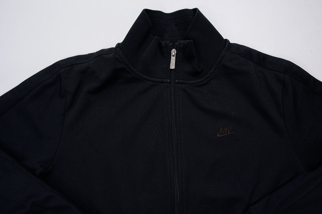 Nike track jacket in black featuring an embroidered swoosh logo on the chest, full view