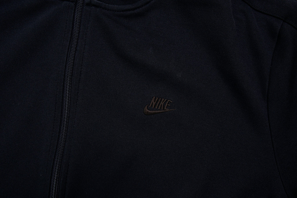 Nike track jacket in black featuring an embroidered swoosh logo on the chest, detail