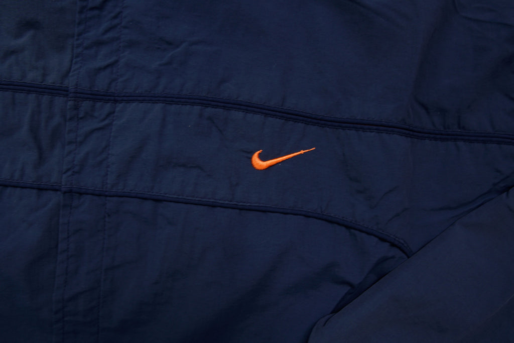 Nike jacket in navy featuring an embroidered orange Swoosh on the chest, detail