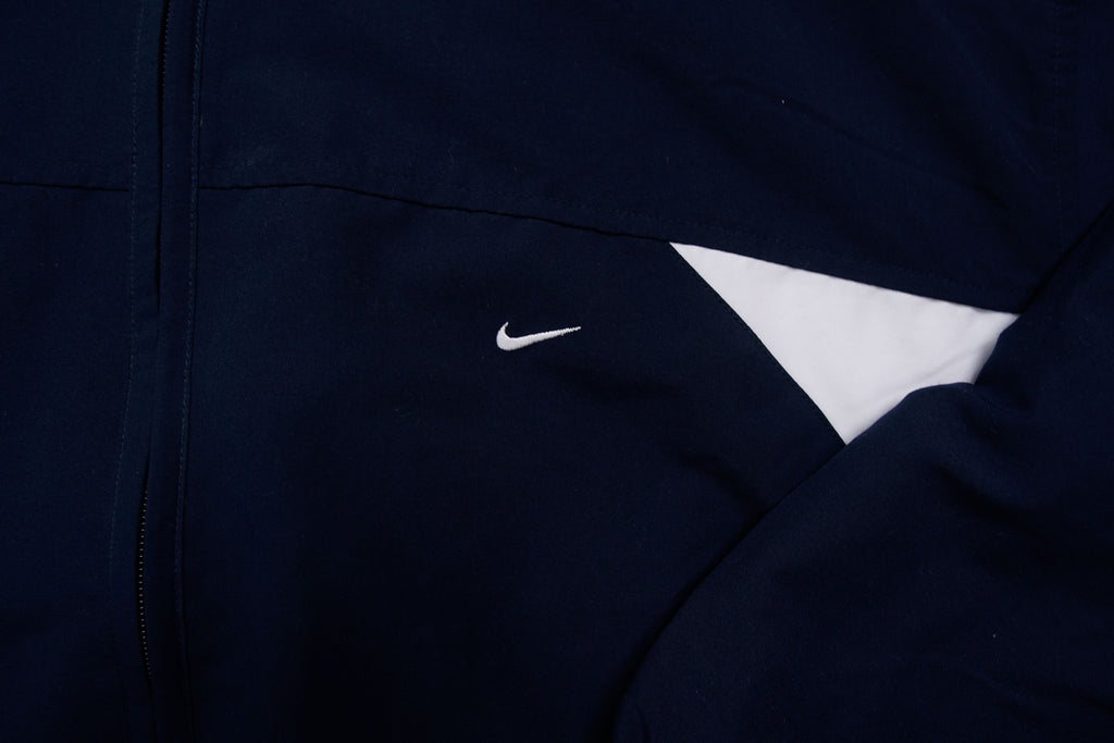 Nike zip-up track jacket in navy with red side panels and a small white swoosh logo, detail