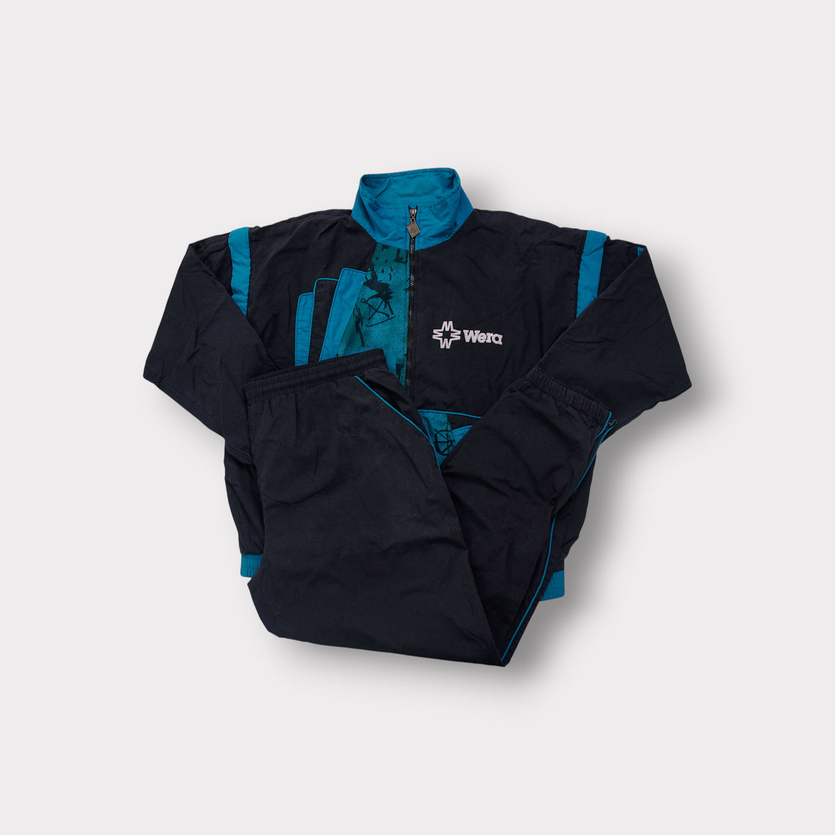 Wera tracksuit in black and teal featuring a front zip and chest embroidery.